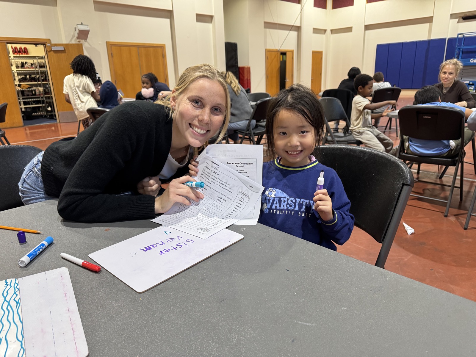 A volunteer and a young learner smiling together over a worksheet
