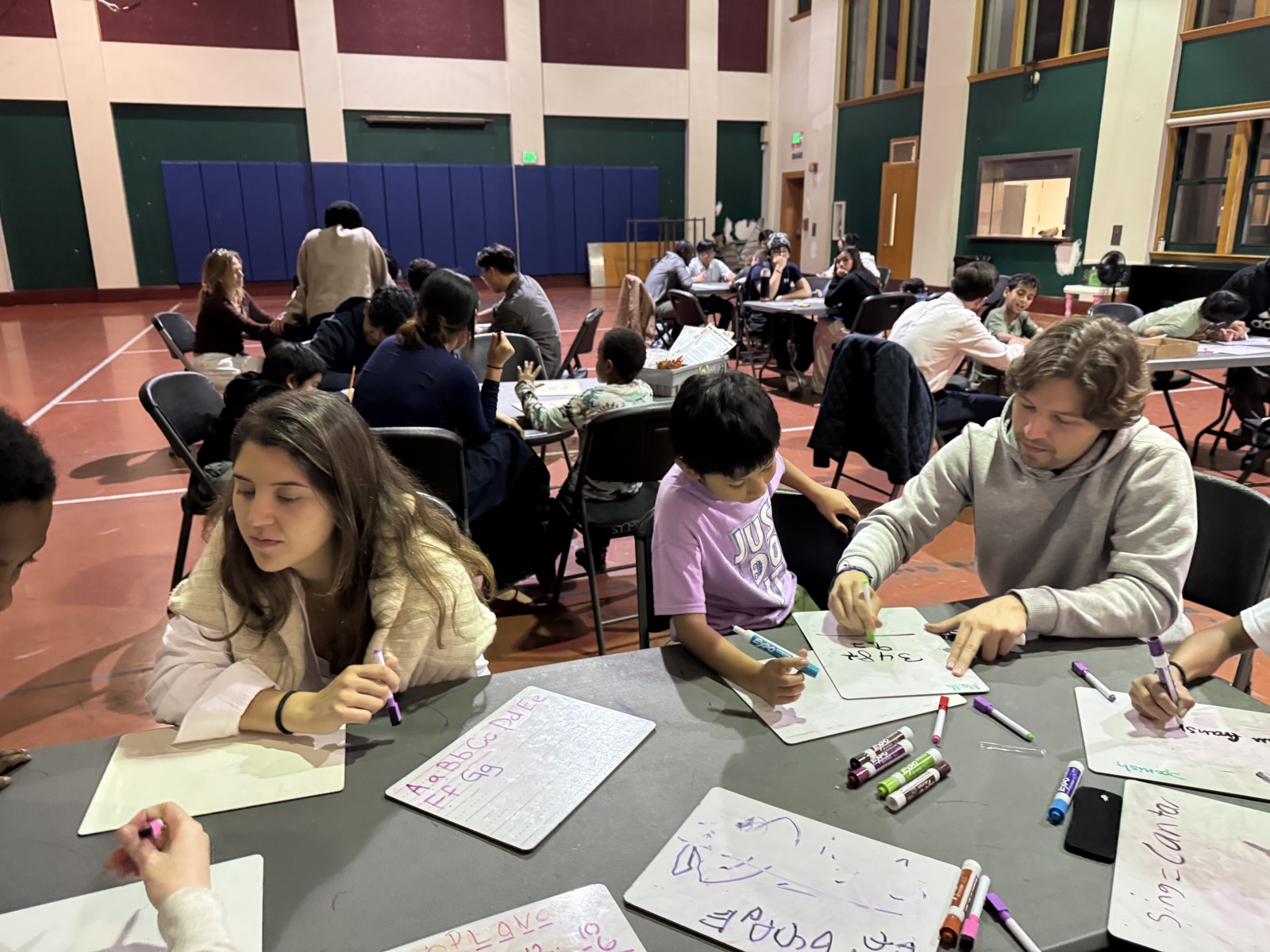 Volunteers and children writing and drawing on whiteboards in the community hall