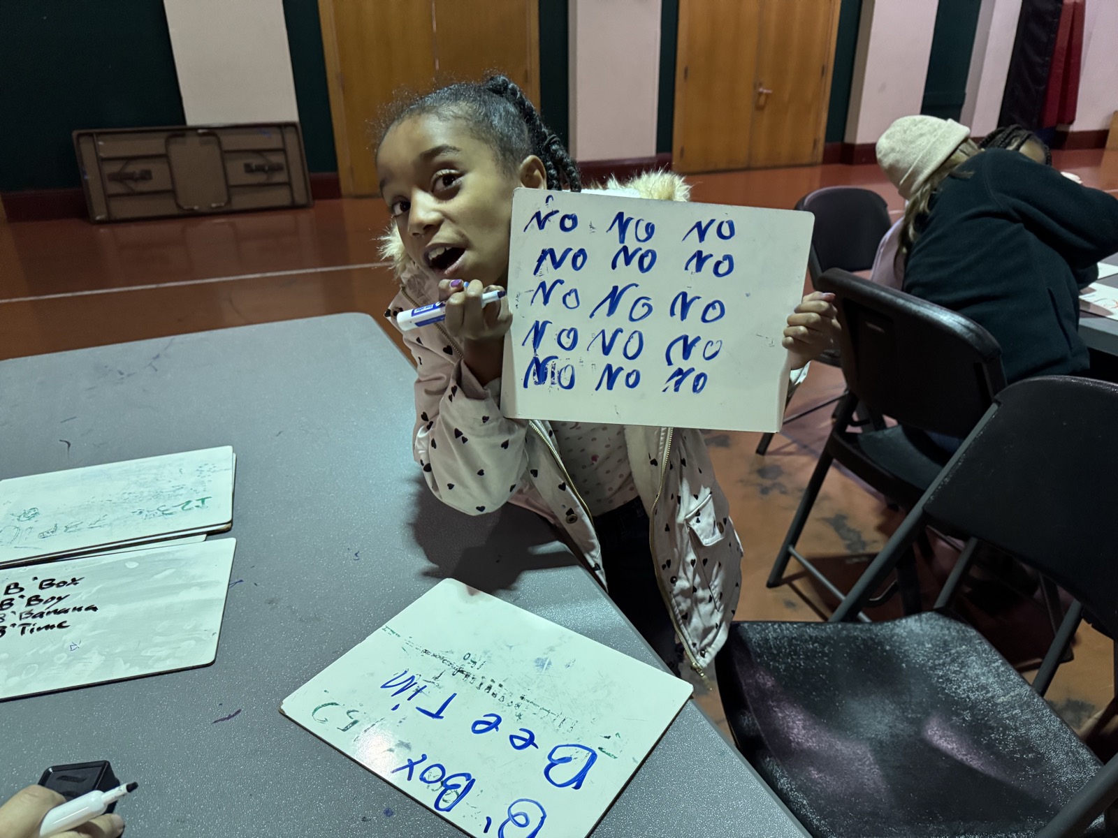 A child laughing while holding up a whiteboard they filled with writing