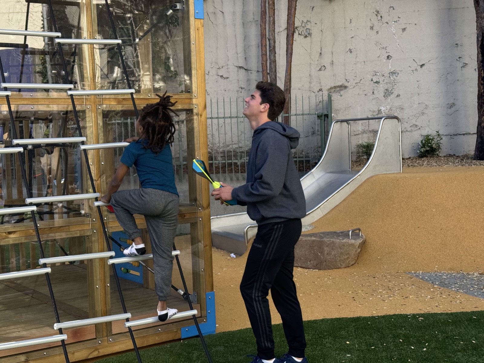 A volunteer cheering on a child climbing the playground structure