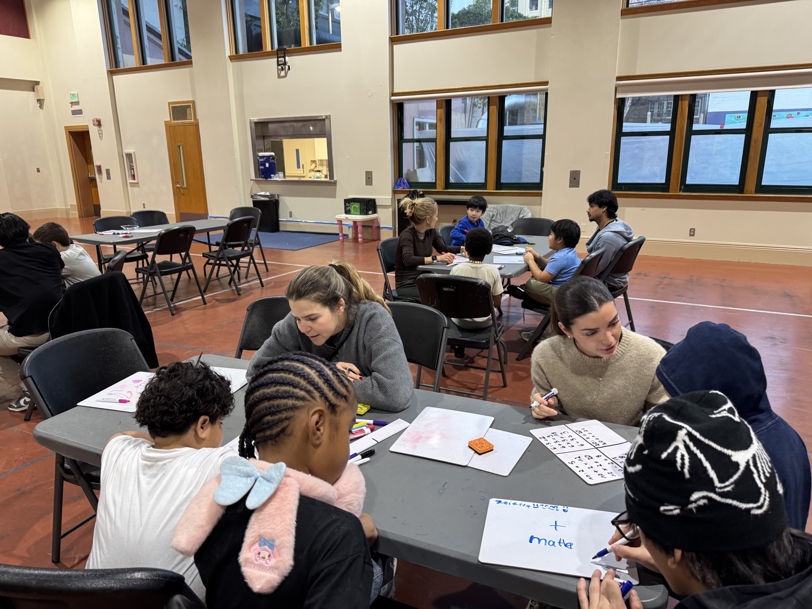 Two volunteers helping children with worksheets in the community hall